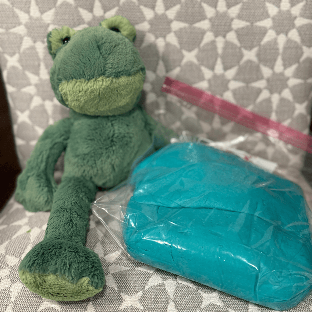Stuffed frog toy next to a ball of teal play dough for kids' sensory play